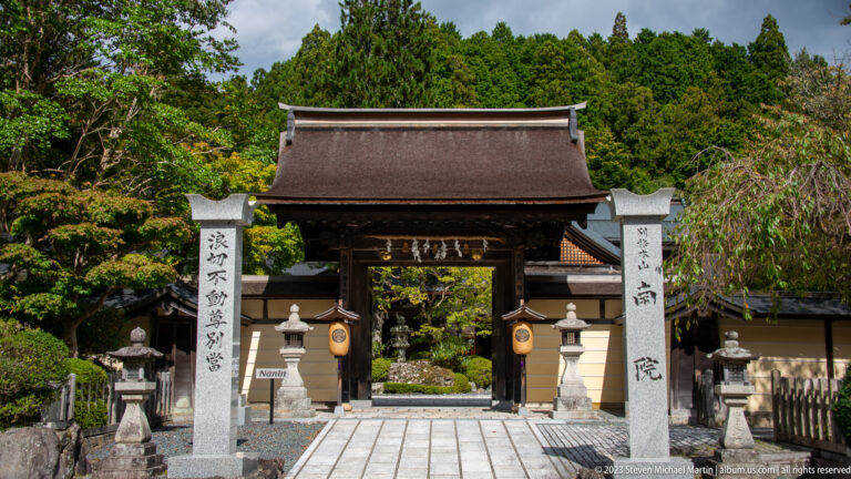 Nanin temple gate between inscribed stone pillars with lanterns and a paved approach.
