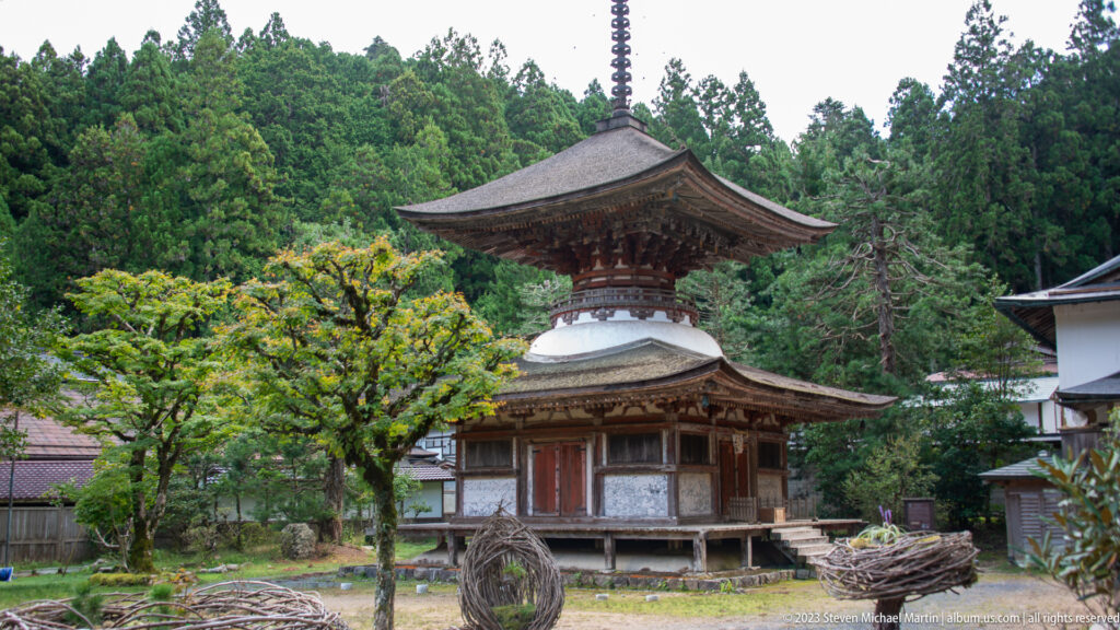 Small two-story pagoda with white lower section, dark timber upper story, and tall finial among trees.