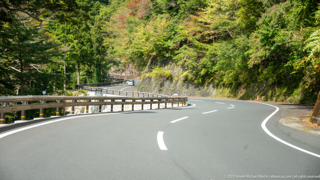 Curving two-lane mountain road with guardrails passing through dense forest near Koyasan.