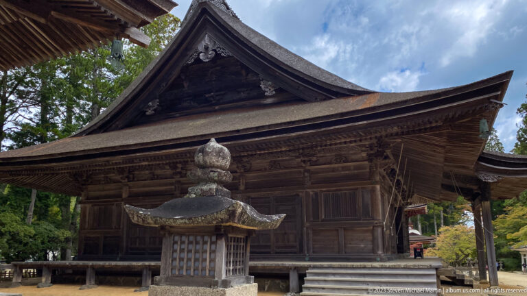 Dark wooden temple hall with deep eaves and a stone lantern in the foreground.