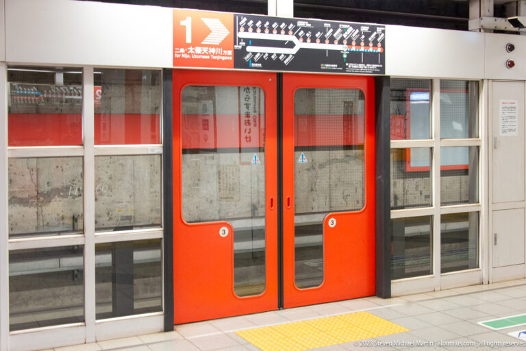 Red platform screen doors in a subway station in its surrounding Kyoto setting.