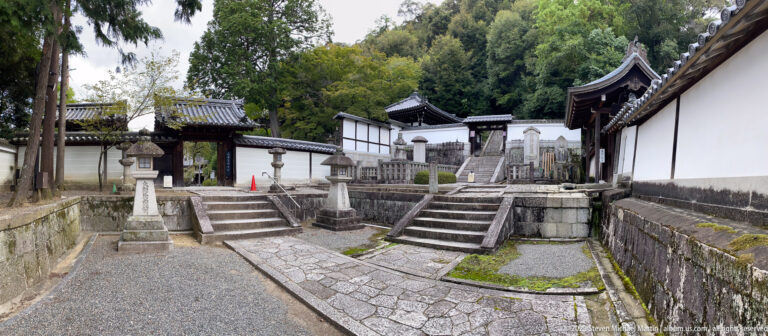 Stone paths and temple buildings in a walled precinct in its surrounding Kyoto setting.