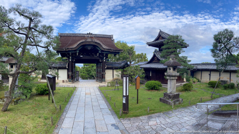 Stone path leading to a wooden temple gate in its surrounding Kyoto setting.