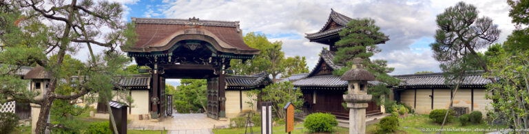 Historic wooden temple gate viewed from the approach in its surrounding Kyoto setting.