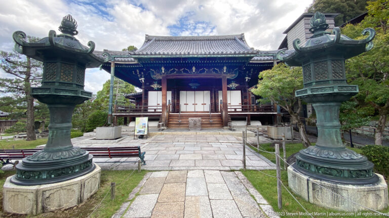 Temple hall beyond bronze lanterns in its surrounding Kyoto setting.