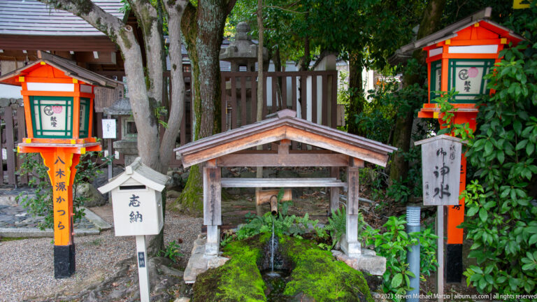 Roofed purification basin with moss-covered stonework and shrine lanterns.
