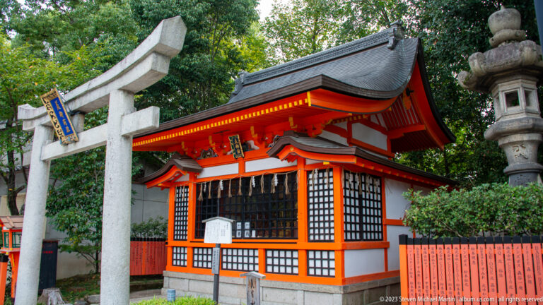 Small vermilion shrine behind a stone torii within the Yasaka Shrine grounds.