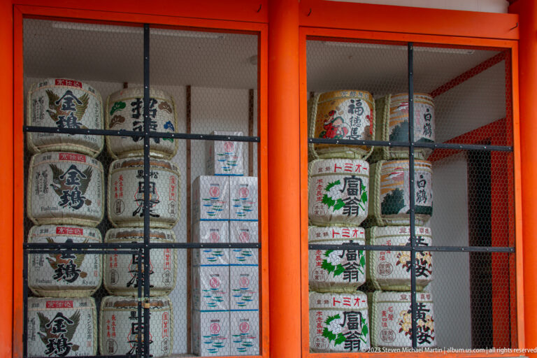 Decorated sake barrels with Japanese labels stacked behind a protective screen.