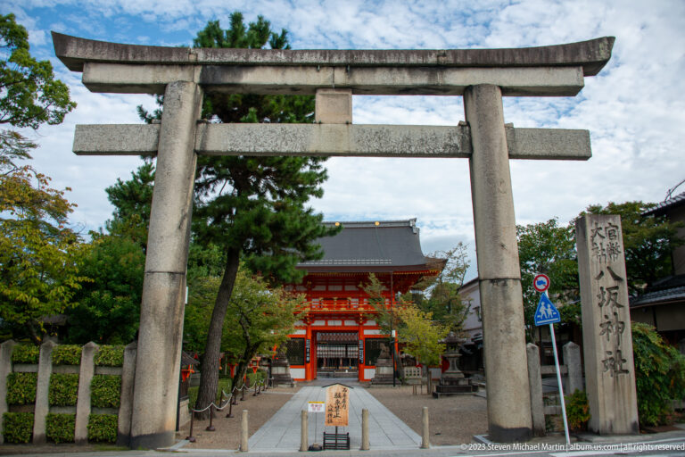 Large stone torii framing the approach to a vermilion gate at Yasaka Shrine.
