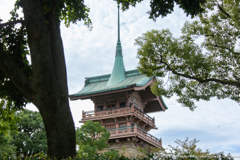 Upper stories of Gionkaku with green copper roof and tall spire above trees.