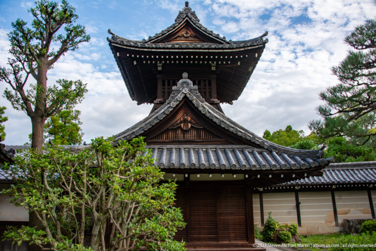 Traditional wooden bell tower above temple walls and garden.