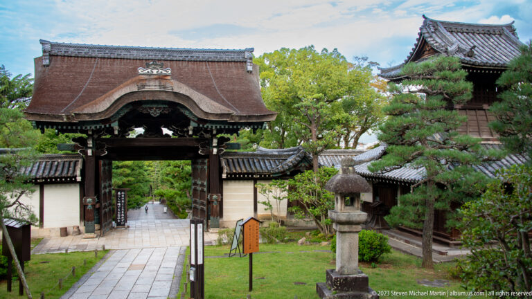 Historic timber gate opening onto a stone path through temple grounds.
