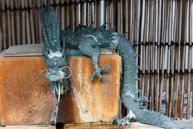 Bronze dragon water spout with scaled body and open mouth above a stone basin.