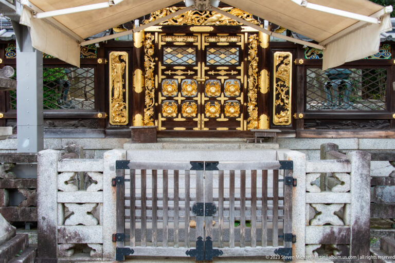 Gilded shrine entrance behind a low stone fence in its surrounding Kyoto setting.