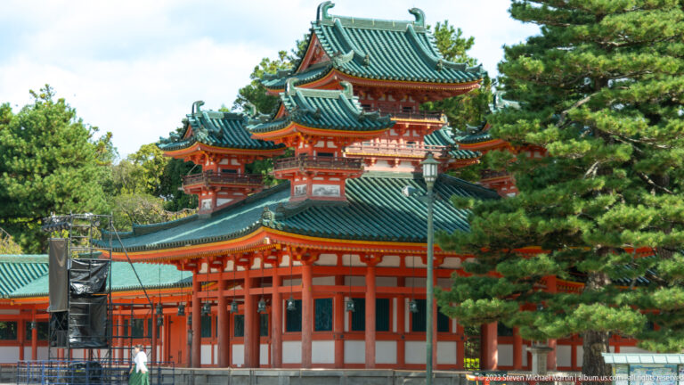 Layered vermilion shrine buildings with green roofs in its surrounding Kyoto setting.