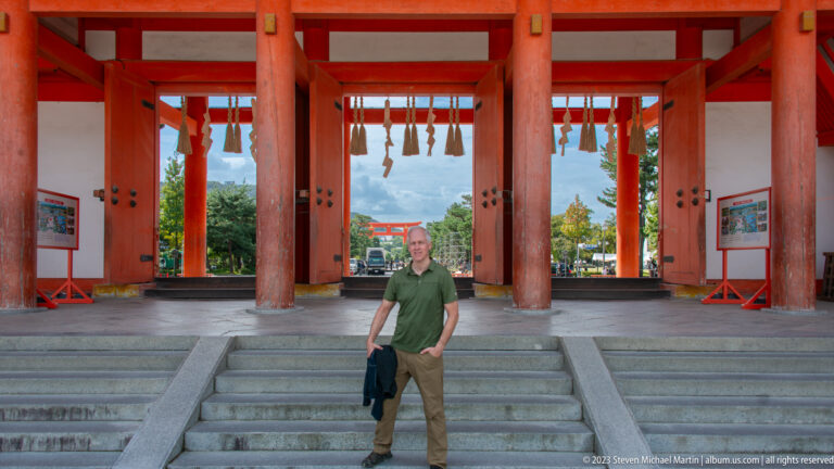 Visitor beneath large vermilion shrine gate in its surrounding Kyoto setting.