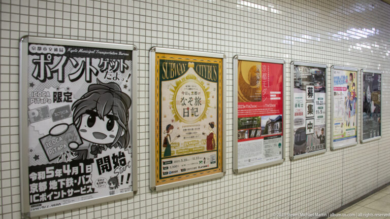 Row of posters mounted on a tiled subway wall in its surrounding Kyoto setting.