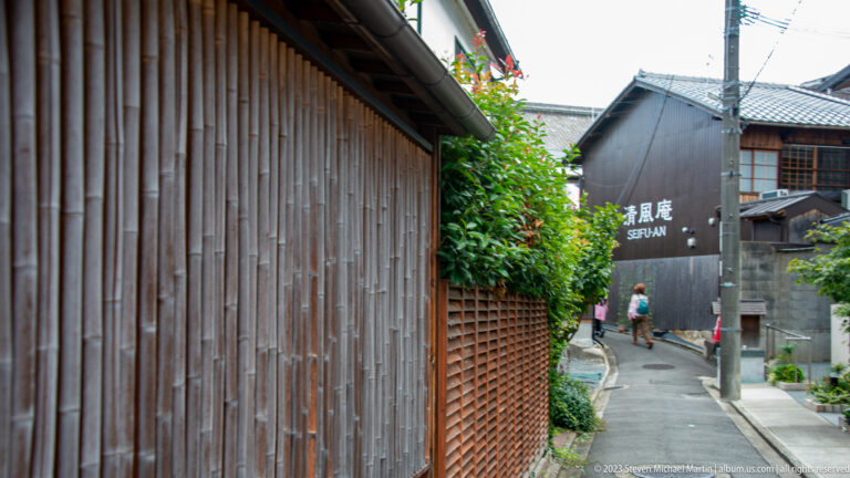 Narrow Gion lane lined with dark wooden machiya façades and greenery in its surrounding Kyoto setting.