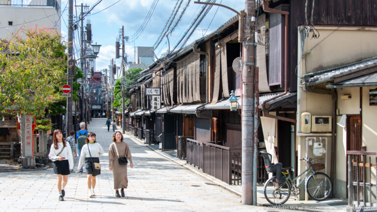 Pedestrians on a narrow Gion street lined with traditional wooden machiya buildings.