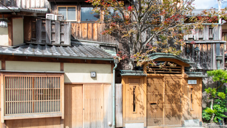 Decorative wooden machiya entrance in Gion with lattice screens, tiled eaves, and a carved transom.