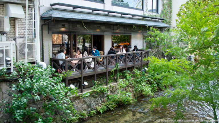 Outdoor restaurant terrace beside a canal in its surrounding Kyoto setting.