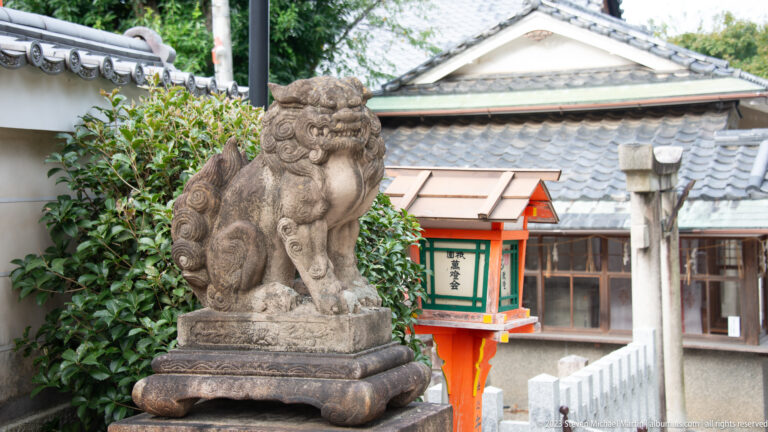 Stone komainu guardian on a pedestal beside a small vermilion shrine.