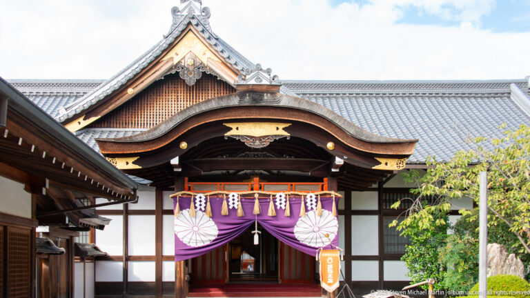 Shrine entrance with purple curtain and sacred ropes in its surrounding Kyoto setting.