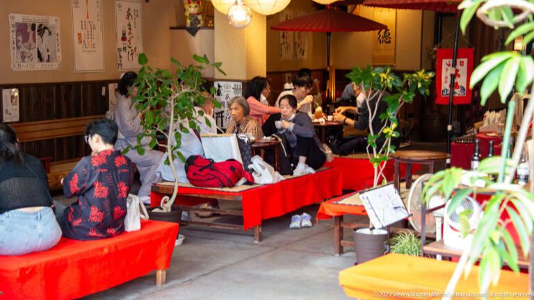 People seated inside a traditional café with red benches in its surrounding Kyoto setting.