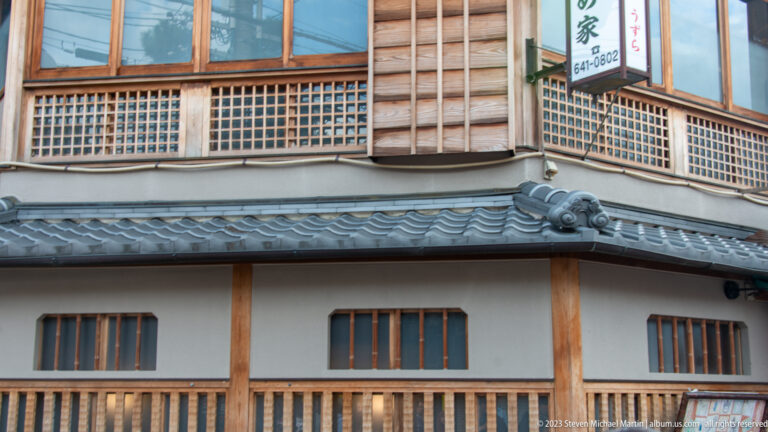 Traditional machiya façade with lattice windows in its surrounding Kyoto setting.