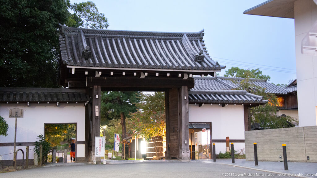 Traditional wooden gate with gray tiled roof between white walls and modern buildings at Chion-in.