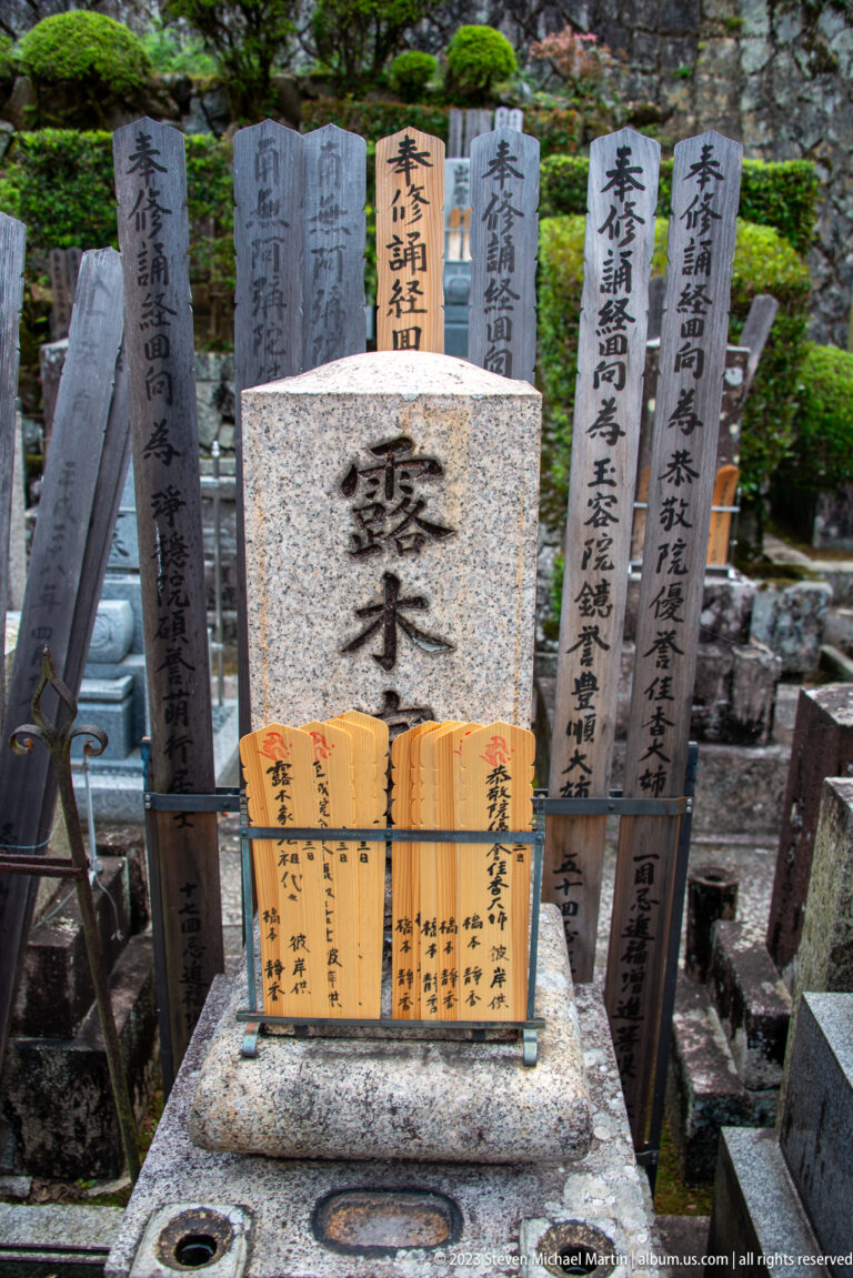 Polished Japanese family grave surrounded by tall inscribed wooden sotōba and smaller memorial tablets in front.
