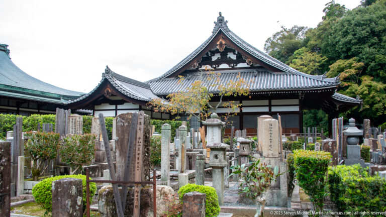 Dense Buddhist cemetery in front of a white-and-dark timber temple building with a tiled gabled roof.