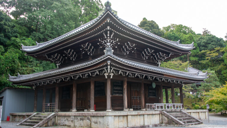 Large dark wooden Buddhist hall on a raised platform with broad tiled roof, deep eaves, and veranda.