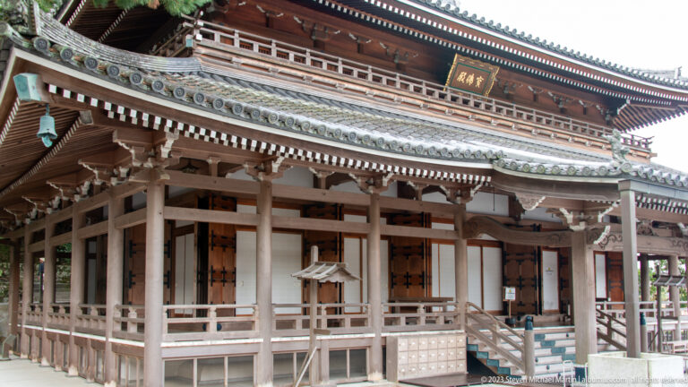 Large light-wood temple hall with deep veranda, layered tiled roof, white panels, and a gilded plaque under the eaves.