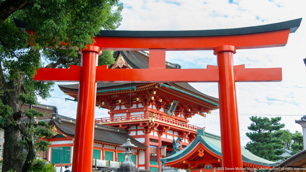 Large vermilion torii framing the upper story and tiled roof of Fushimi Inari Taisha’s Rōmon gate.