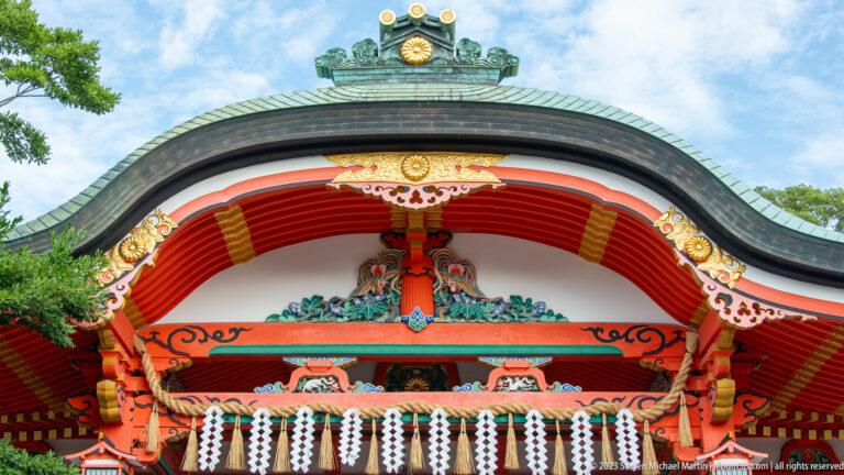 Close view of an ornate curved shrine gable with gilded details, painted carving, and white paper streamers.