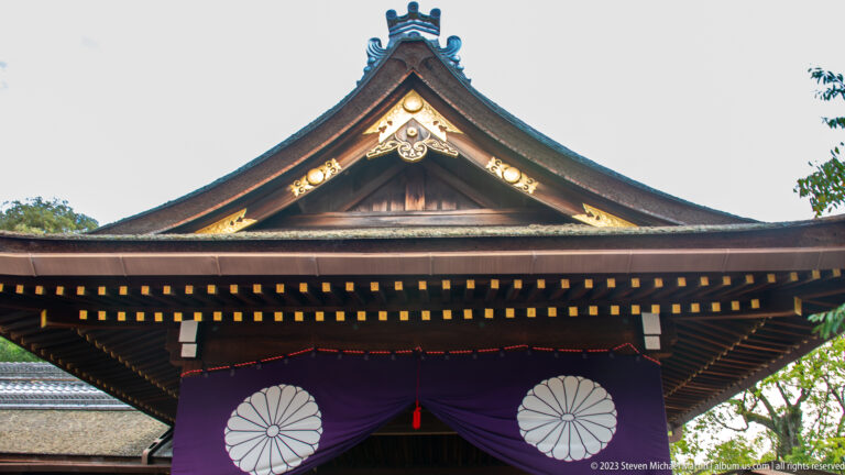 Steep shrine gable above purple curtains decorated with two large white chrysanthemum crests.
