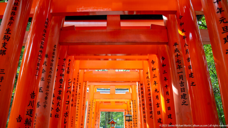 View through repeating vermilion torii with black inscriptions toward a distant shrine.