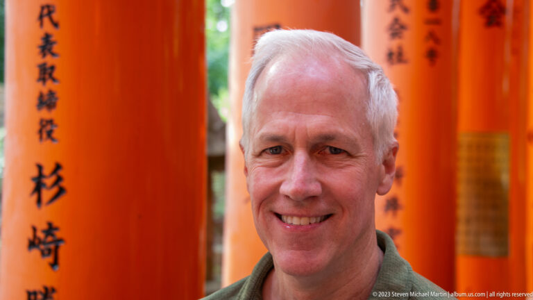Smiling visitor standing before softly blurred vermilion torii.