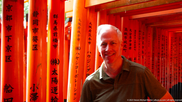Smiling visitor standing among vermilion torii marked with black donor inscriptions.
