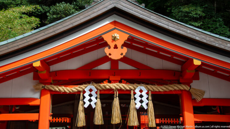 Shrine gable with shimenawa rope, white shide streamers, and vermilion beams.