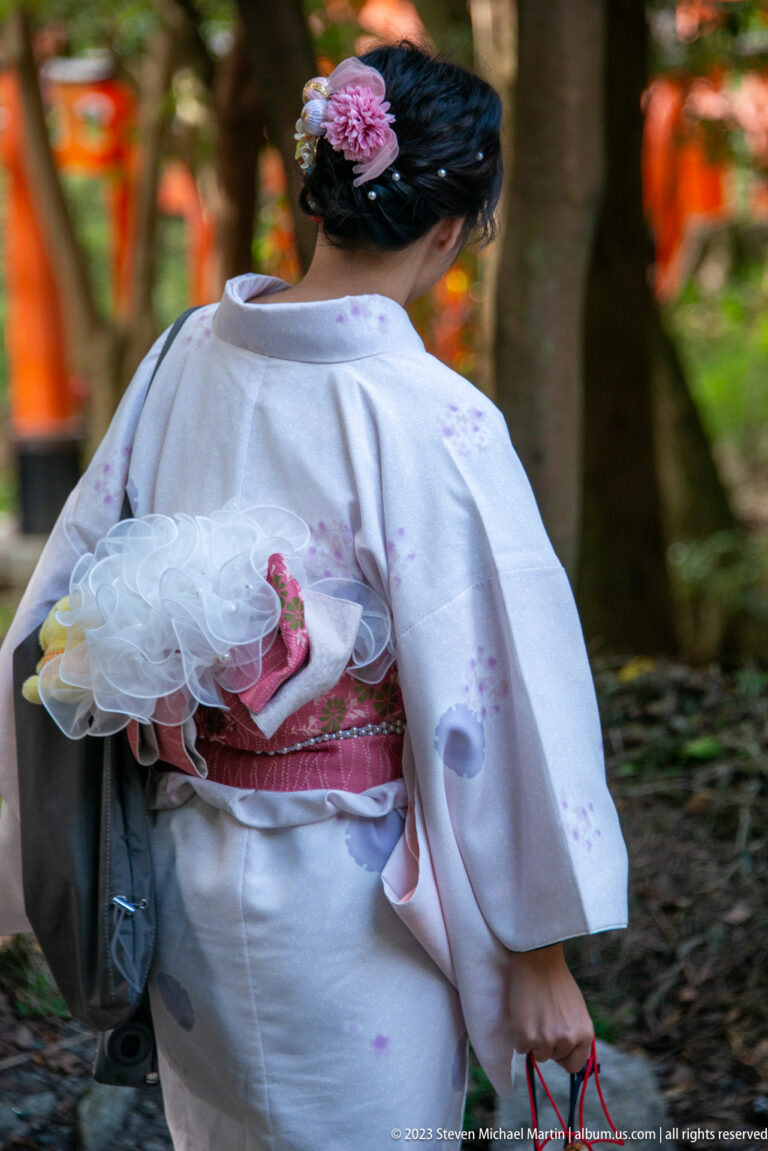 Rear view of a visitor wearing a pale kimono with an elaborate obi and floral hair ornament.