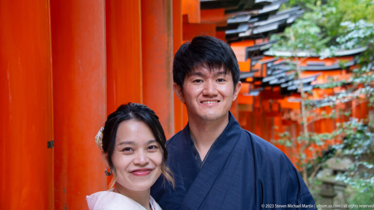 Smiling couple in traditional clothing posing before vermilion torii.