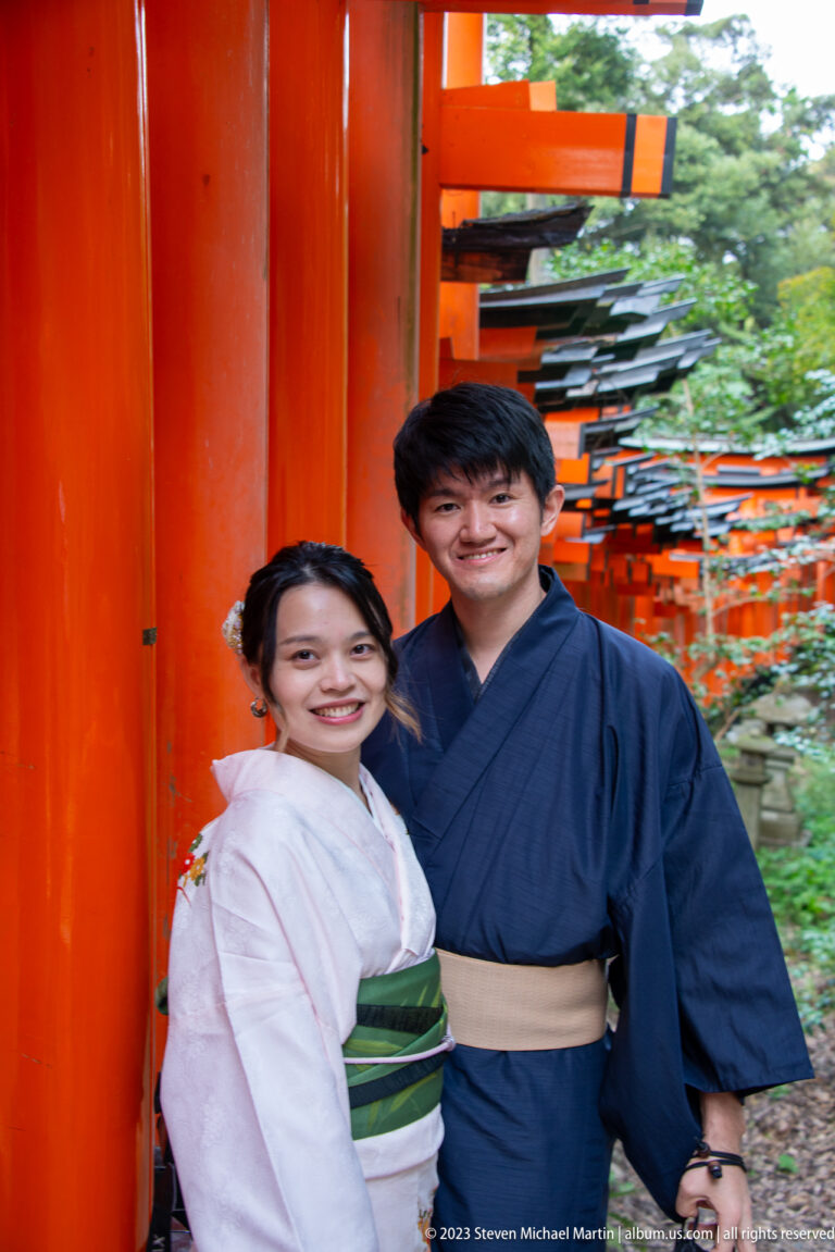 Smiling couple in traditional clothing posing beside vermilion torii.
