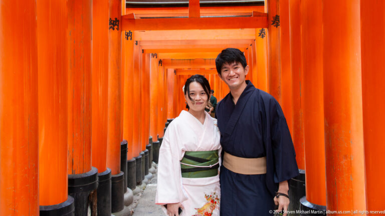 Couple in traditional clothing standing inside a corridor of vermilion torii.