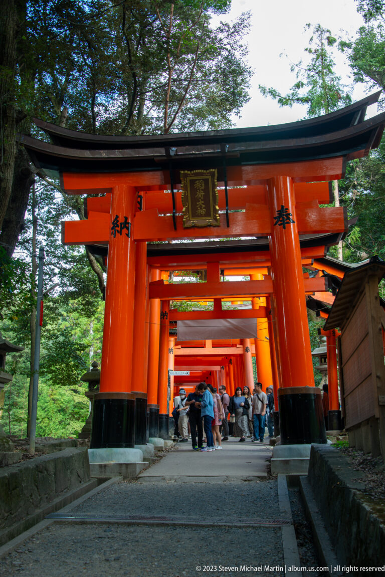 Large vermilion torii with a dedication plaque framing visitors and additional shrine gates beyond.