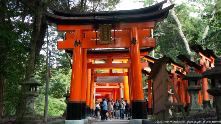 Oblique view of a vermilion torii with dedication plaque and successive gates beyond.