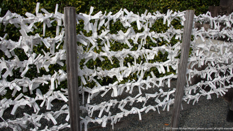Rows of folded white paper fortunes tied to racks at a shrine.