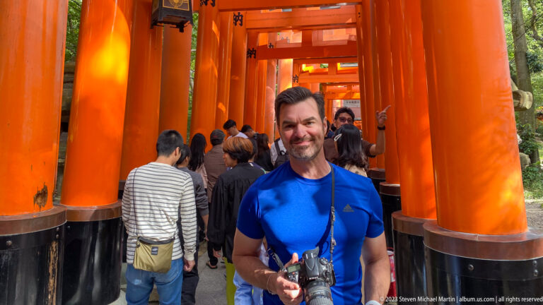 Photographer holding a camera inside a corridor of vermilion torii.