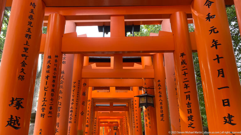 Inscribed vermilion torii with a hanging lantern in the corridor.